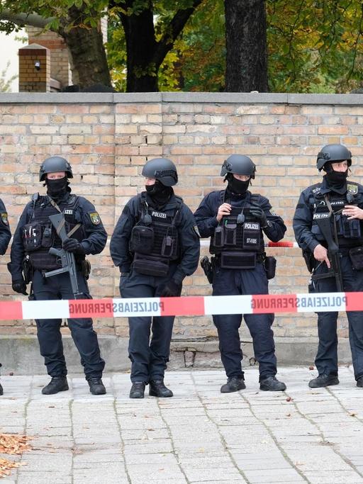 Polizisten mit Schutzhelmen sichern den Bereich am jüdischen Friedhof in Halle. 