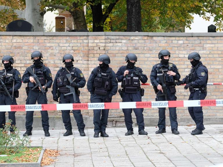 Polizisten mit Schutzhelmen sichern den Bereich am jüdischen Friedhof in Halle. 