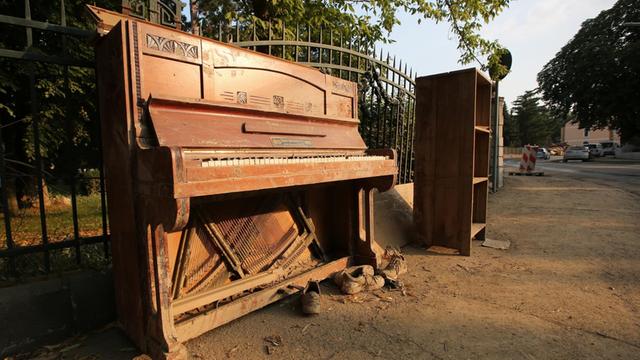 Ein kaputtes Klavier steht an einer Straße.