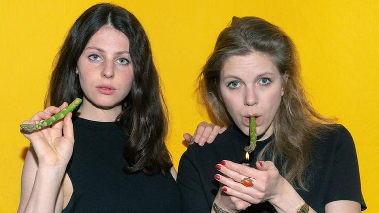 Foto zum Stück "Keine Ahnung" an den Sophiensaelen in Berlin. Zwei Frauen haben jeweils eine Spargelstange wie eine Zigarette in der Hand. Foto zum Stück "Keine Ahnung" an den Sophiensaelen in Berlin. Zwei Frauen haben jeweils eine Spargelstange wie eine Zigarette in der Hand.