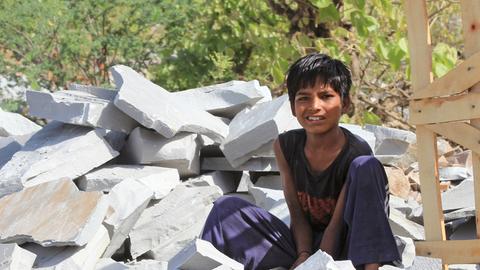 Ein kleiner Junge sitzt in Kota, in der indischen Provinz Rajasthan, neben einem Transportgestell aus Holz auf einem Haufen Steine. Tausende Kinder hauen in Steinbrüchen in Indien Pflastersteine für den europäischen Markt.