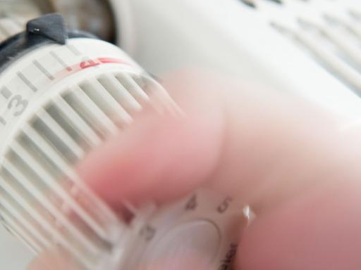 Jemand dreht an einem Thermostat eines Heizkörpers.