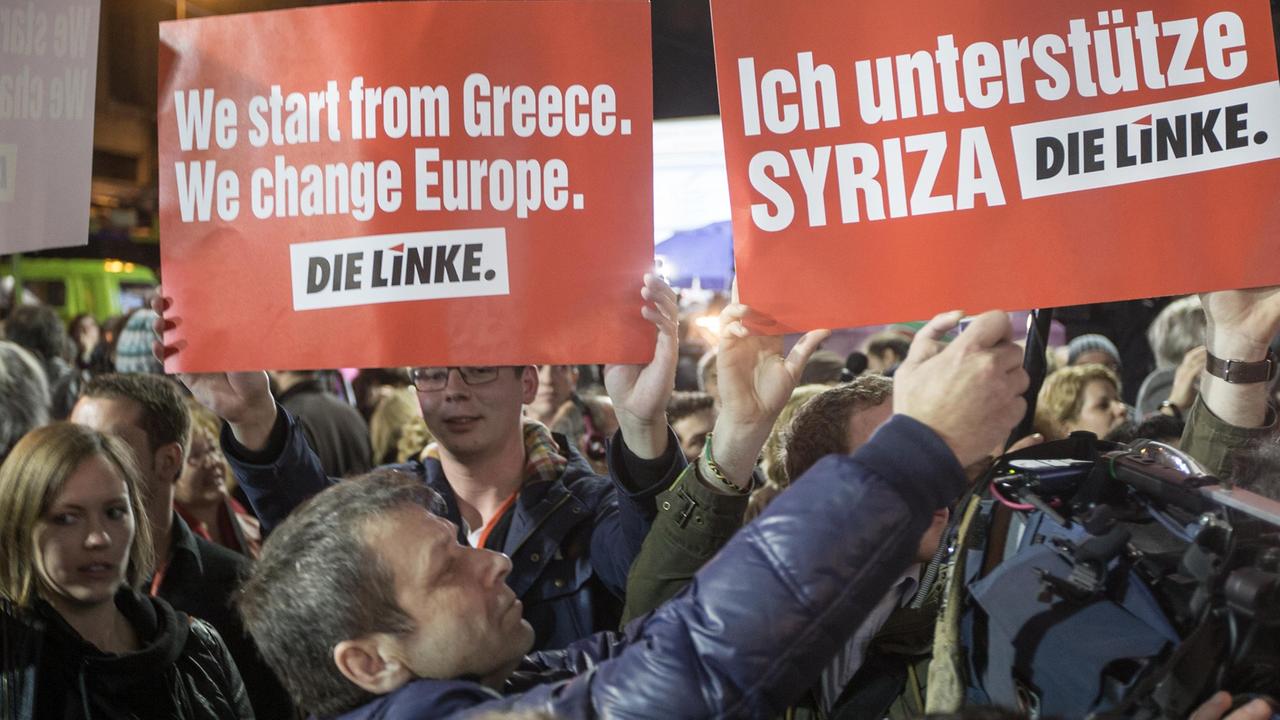 In einer Menschenmenge halten Griechen zwei Schilder der Linkspartei hoch, auf denen u.a. steht: "Ich unterstütze Syriza". In einer Menschenmenge halten Griechen zwei Schilder der Linkspartei hoch, auf denen u.a. steht: "Ich unterstütze Syriza".