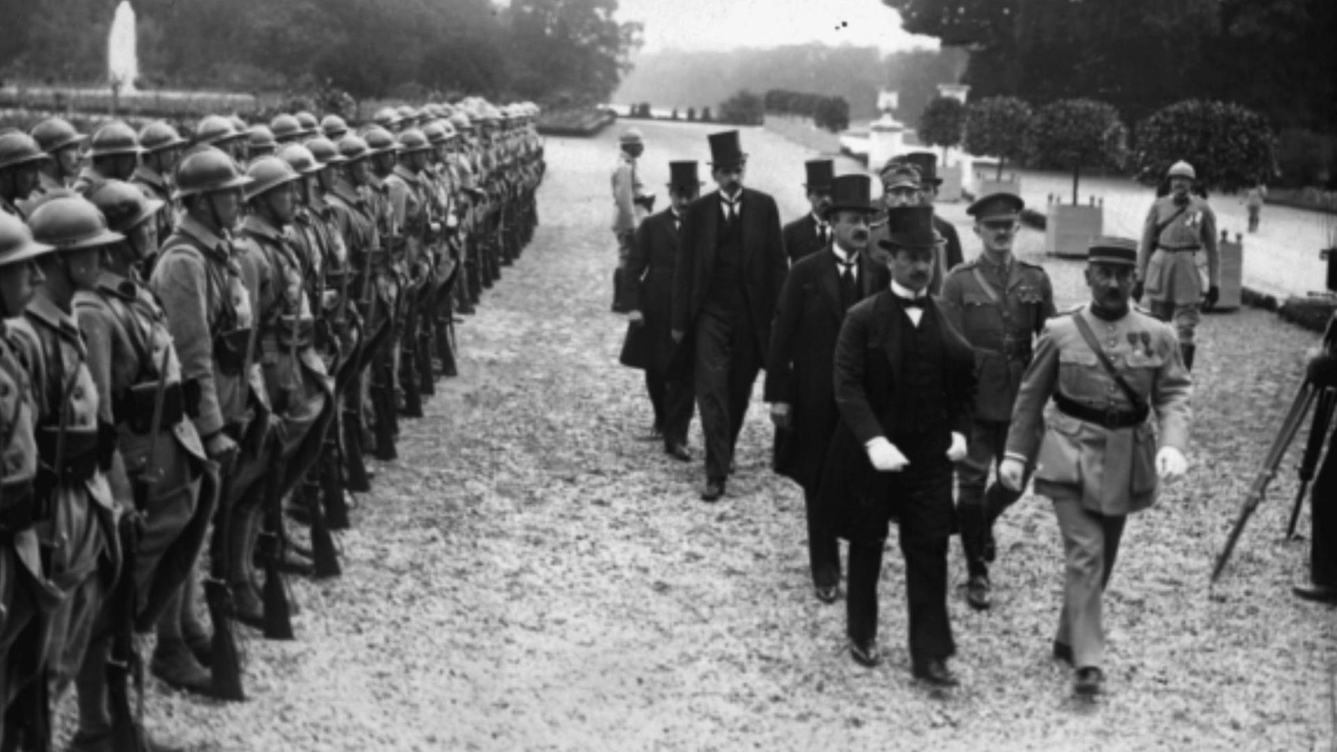 Ankunft der ungarischen Delegation, unter Führung von Dr. Benard, begleitet von Colonel Henry. Männer in Anzügen laufen an Soldatenreihen vorbei. Ankunft der ungarischen Delegation, unter Führung von Dr. Benard, begleitet von Colonel Henry. Männer in Anzügen laufen an Soldatenreihen vorbei.