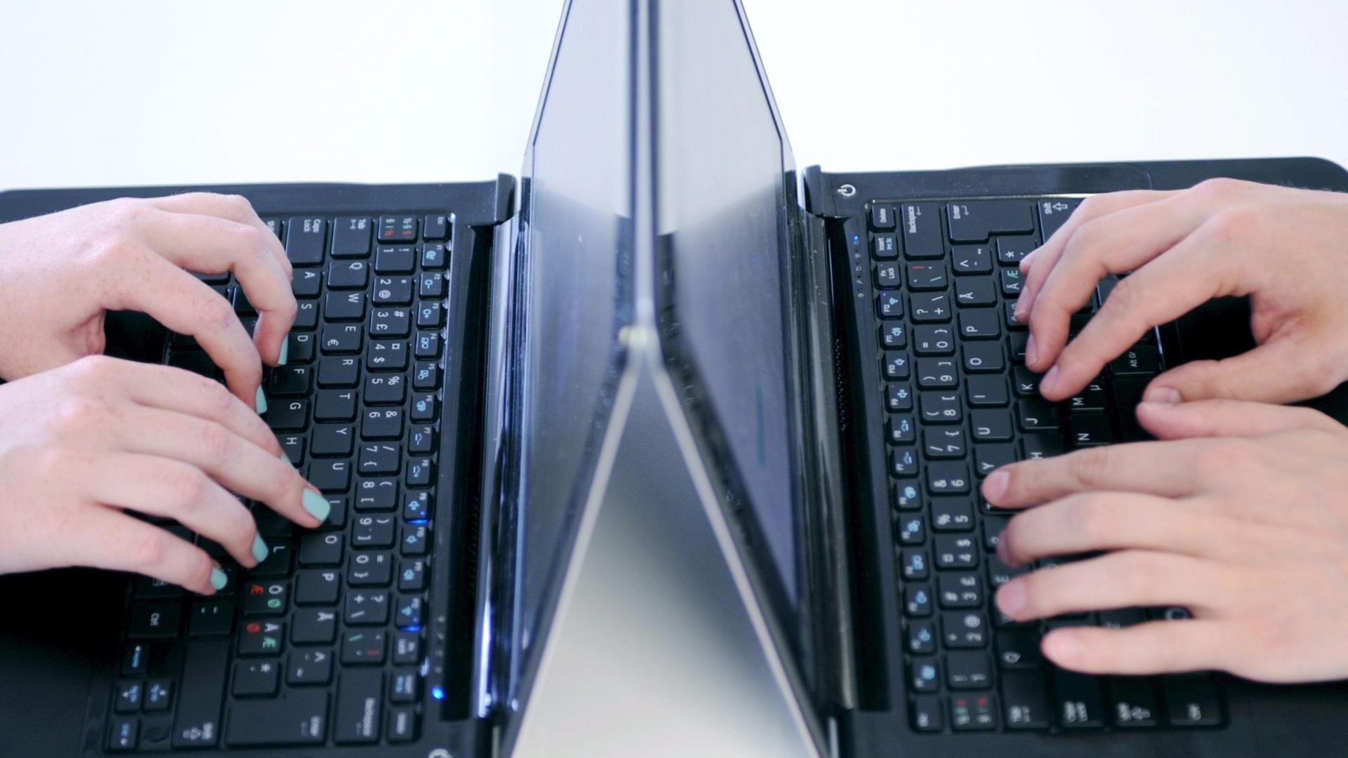 Zwei Laptops stehen sich gegenüber. Hände tippen darauf. Zwei Laptops stehen sich gegenüber. Hände tippen darauf.