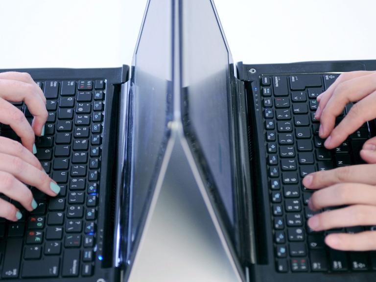 Zwei Laptops stehen sich gegenüber. Hände tippen darauf.