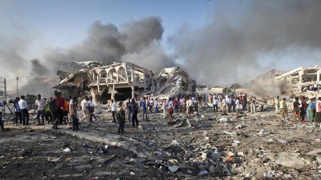 Menschen suchen am in Mogadischu (Somalia) nach einem Selbstmordanschlag in den Trümmern eines Hauses nach Überlebenden. Über ihnen sind Rauchsäulen ztu sehen.