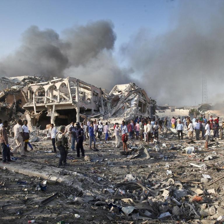 Menschen suchen am in Mogadischu (Somalia) nach einem Selbstmordanschlag in den Trümmern eines Hauses nach Überlebenden. Über ihnen sind Rauchsäulen ztu sehen.