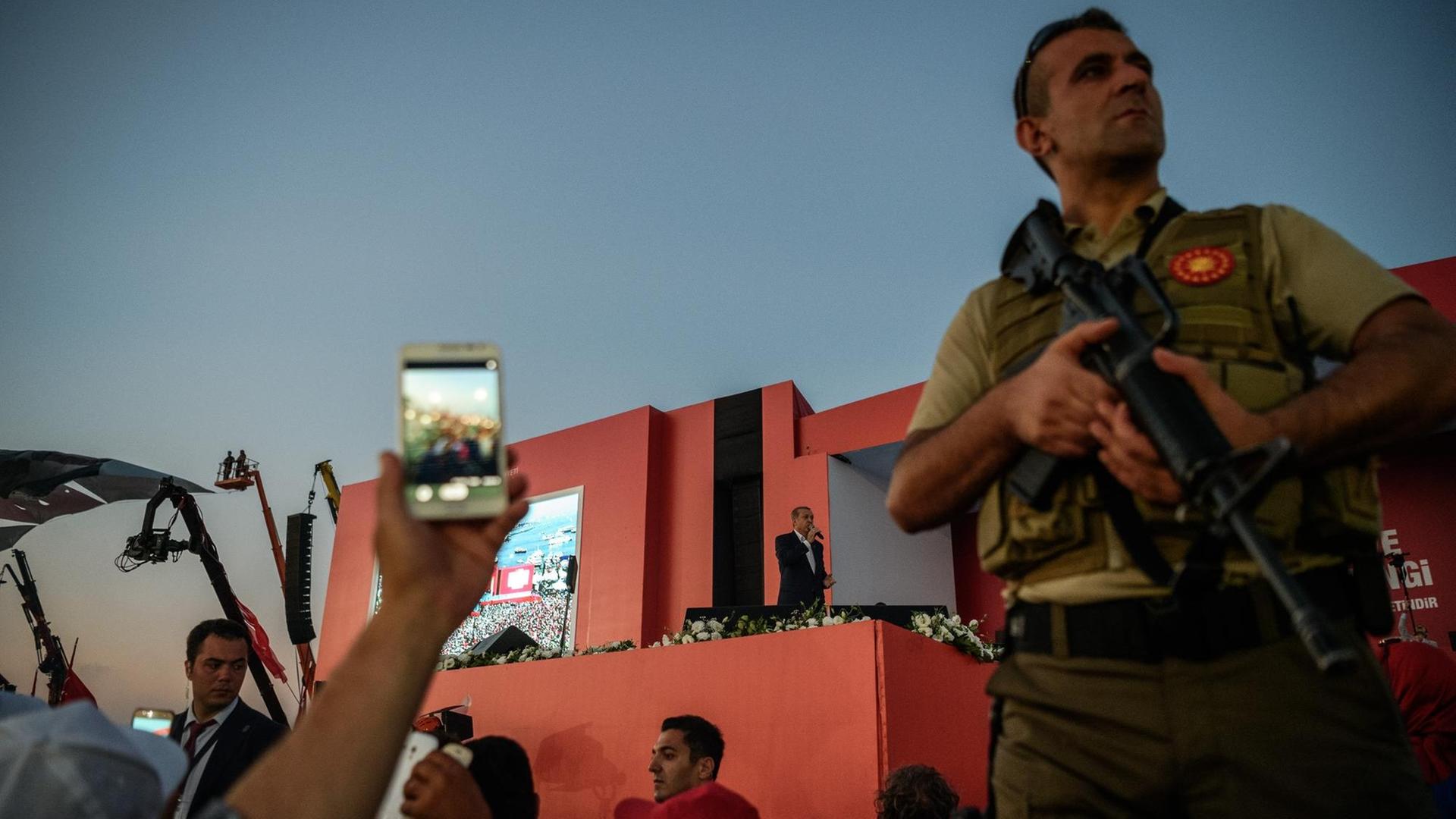 Aufnahme aus dem Publikum. Auf einer Bühne steht der türkische Präsident Recep Tayyip Erdogan. Ein Sicherheitsoffizier überwacht die Zuschauer. Aufnahme aus dem Publikum. Auf einer Bühne steht der türkische Präsident Recep Tayyip Erdogan. Ein Sicherheitsoffizier überwacht die Zuschauer.