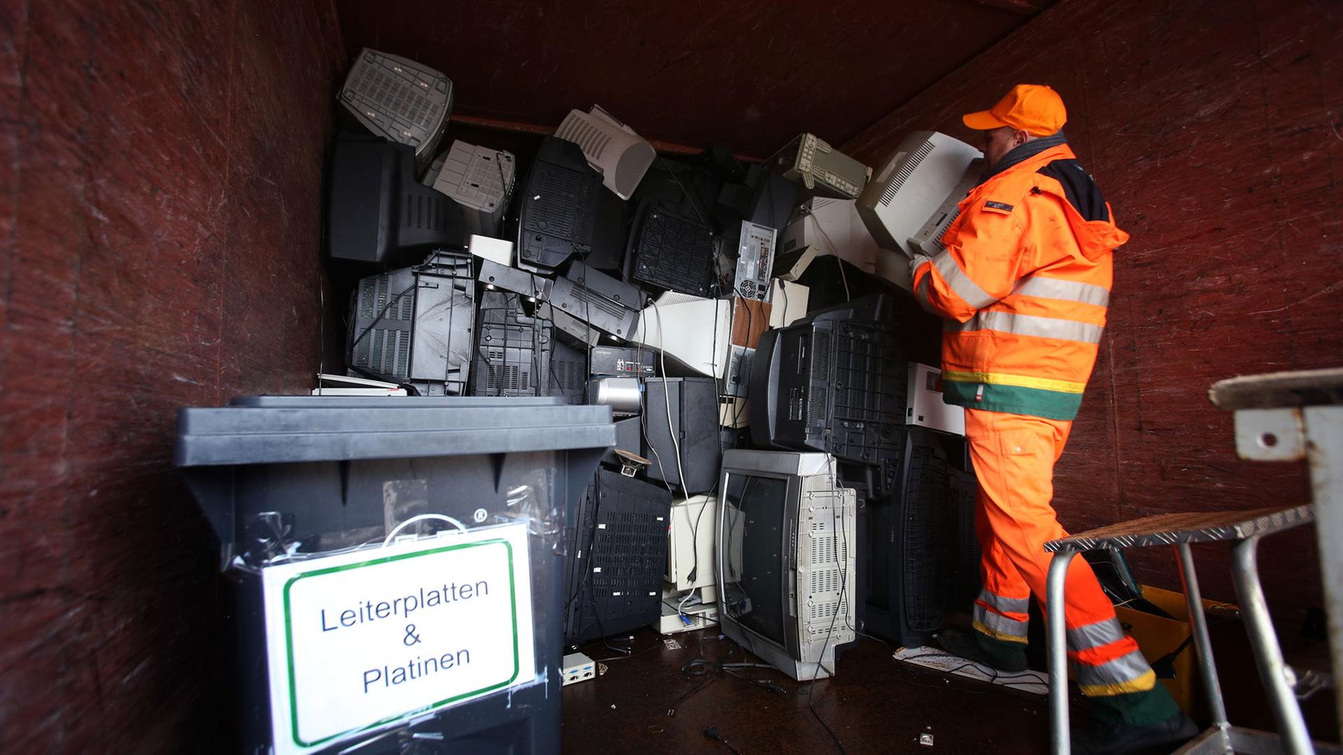 Ein Mitarbeiter der Hamburger Stadtreinigung stapelt am 04.02.2013 ausrangierte Fernseher und Monitore in einem Sammelcontainer für Elektroschrott auf dem Recyclinghof Bahrenfeld in Hamburg.