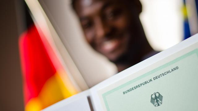 Ein Mann aus Kamerun posiert bei einer Einbürgerungszeremonie für Erinnerungsfotos mit einer Einbürgerungsurkunde der Bundesrepublik Deutschland.