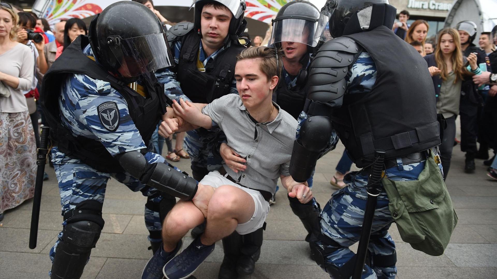 Polizisten in Schutzausrüstung tragen einen jungen Demonstranten davon.