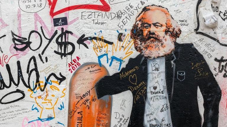Eine Street-Art-Karikatur an einer Wand zeigt Karl Marx als Flaschensammler, der in einem Mülleimer wühlt.