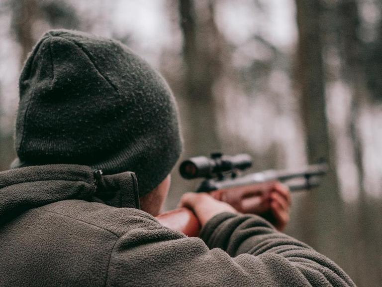 Ein Mann geht im Wald mit einem Gewehr jagen.