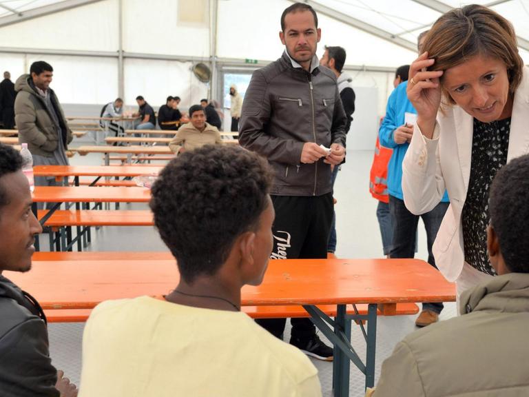 Die rheinland-pfälzische Ministerpräsidentin Malu Dreyer (r, SPD) spricht am 17.08.2015 in einem Aufenthaltszelt auf dem Flughafen Frankfurt-Hahn in Lautzenhausen (Rhein-Hunsrück-Kreis) mit Bewohnern. Auf dem Hahn sind zur Zeit 198 Flüchtlinge der Außenstelle der Aufnahmeeinrichtung für Asylbewerber (AfA) in Ingelheim untergebracht.