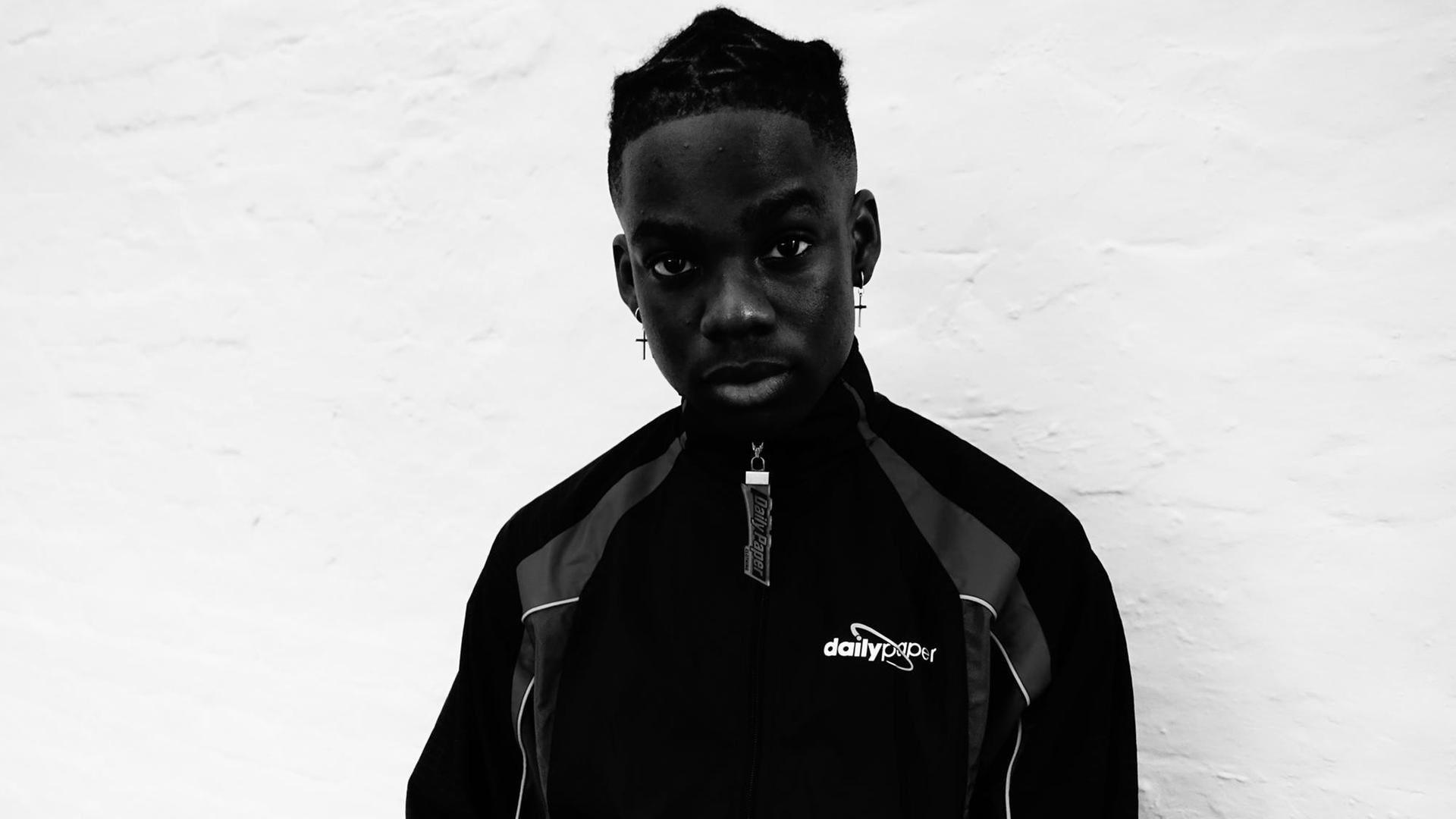 Auf dem Bild ist der afrikanische Rapper Rema zu sehen. Er blickt neugierig in die Kamera Auf dem Bild ist der afrikanische Rapper Rema zu sehen. Er blickt neugierig in die Kamera