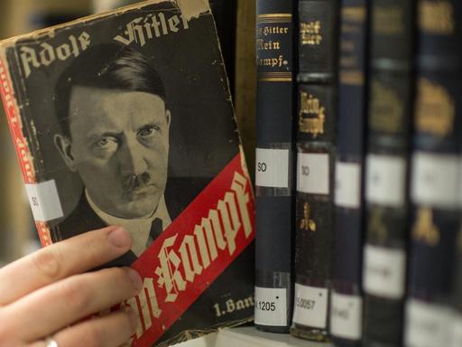 Eine Hand zieht eine Ausgabe von Hitlers "Mein Kampf" aus dem Regal.