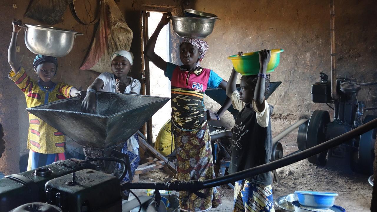 Frauen schütten Nüsse des afrikanischen Butterbaums in ein Mahlwerk.