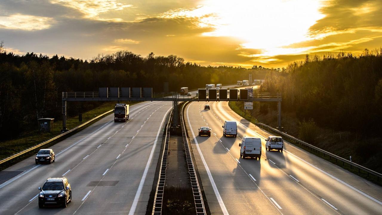 Autos und Lkw fahren beim Sonnenuntergang auf einer Autobahn.