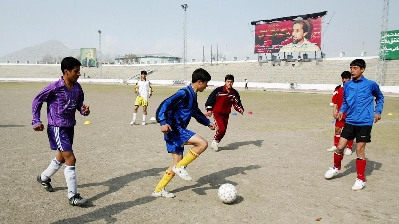 Afghanische Jungen im Stadion in Kabul am 24. Februar 2004. Im Hintergrund ist ein Poster des ehemaligen afghanischen Führers Ahmad Shah Massoud zu sehen, auf dem die Tugenden seines Märtyrertodes gepriesen werden.