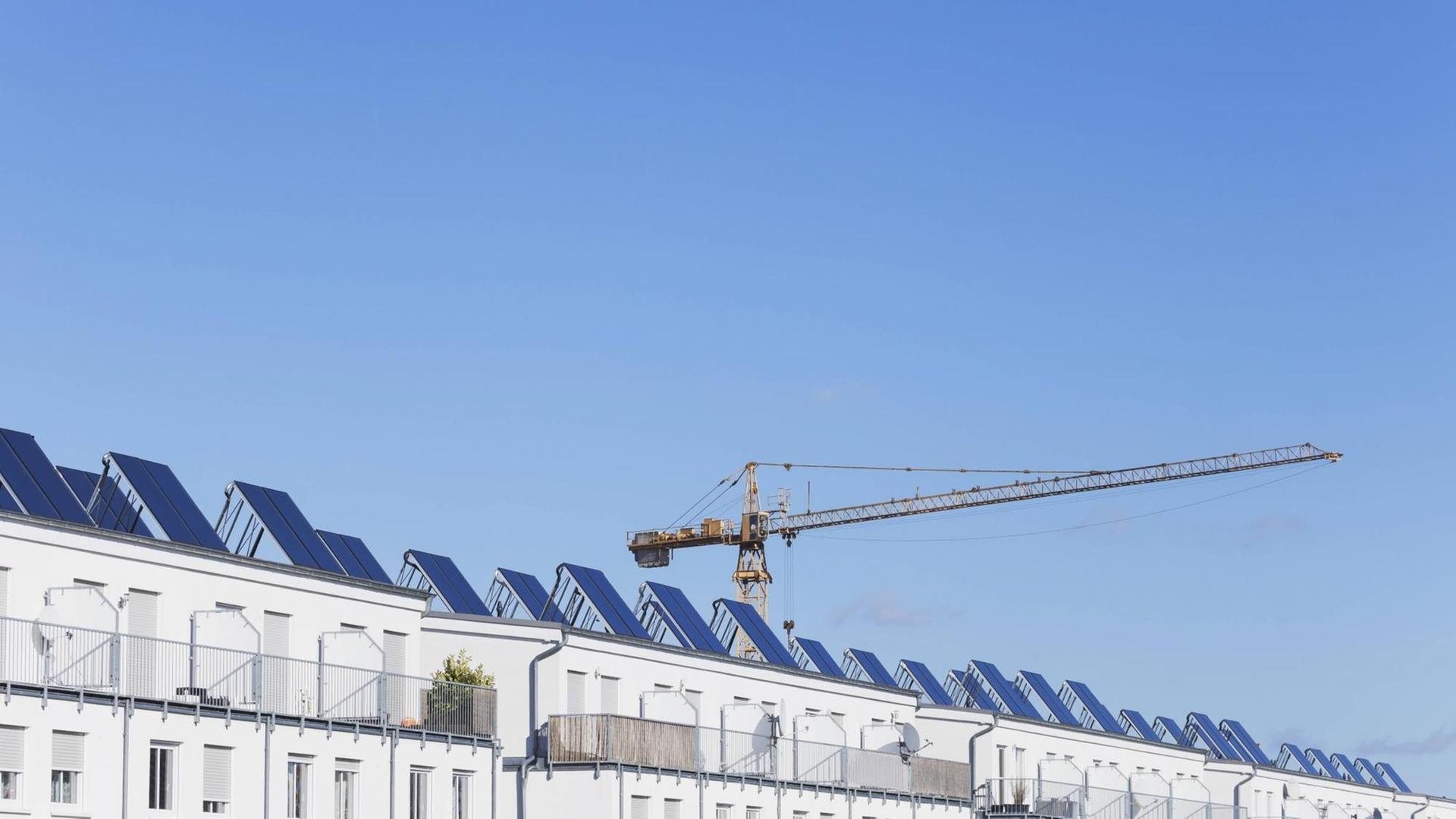 Dachgeschoss eines Neubaus der mit vielen einzeln stehenden Solarpanels bestückt ist. Dahinter ein Baukran. Dachgeschoss eines Neubaus der mit vielen einzeln stehenden Solarpanels bestückt ist. Dahinter ein Baukran.