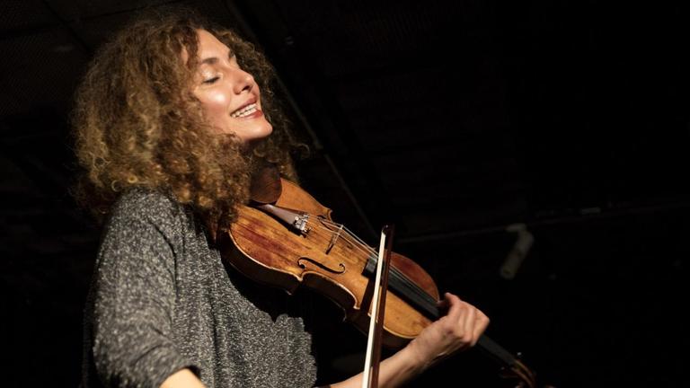 Die Geigerin hält ihr Instrument mit geschlossenen Augen und spielt auf einer dunklen Bühne Die Geigerin hält ihr Instrument mit geschlossenen Augen und spielt auf einer dunklen Bühne