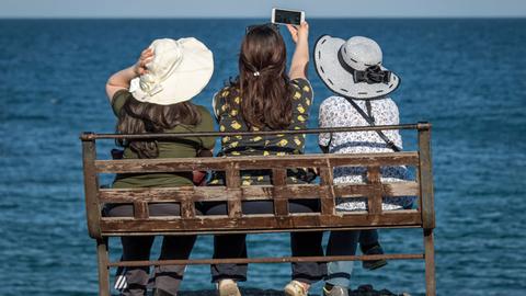 Drei Touristinnen sitzen in Antalya auf einer Bank und blicken aufs Meer.