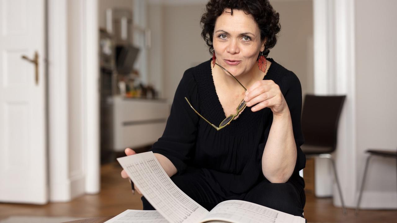 Die Bratscherin sitzt in ihrer Wohnung an einem Tisch und blättert in einer Partitur. Die Bratscherin sitzt in ihrer Wohnung an einem Tisch und blättert in einer Partitur.