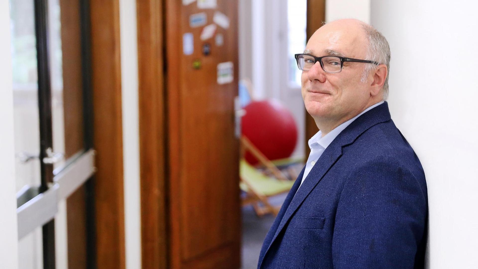Prof. Dr. Wolfgang Schulz lehnt in einem Gang an einer Wand. Im Hintergrund in der Unschärfe eine offene Zimmertür. Prof. Dr. Wolfgang Schulz lehnt in einem Gang an einer Wand. Im Hintergrund in der Unschärfe eine offene Zimmertür.