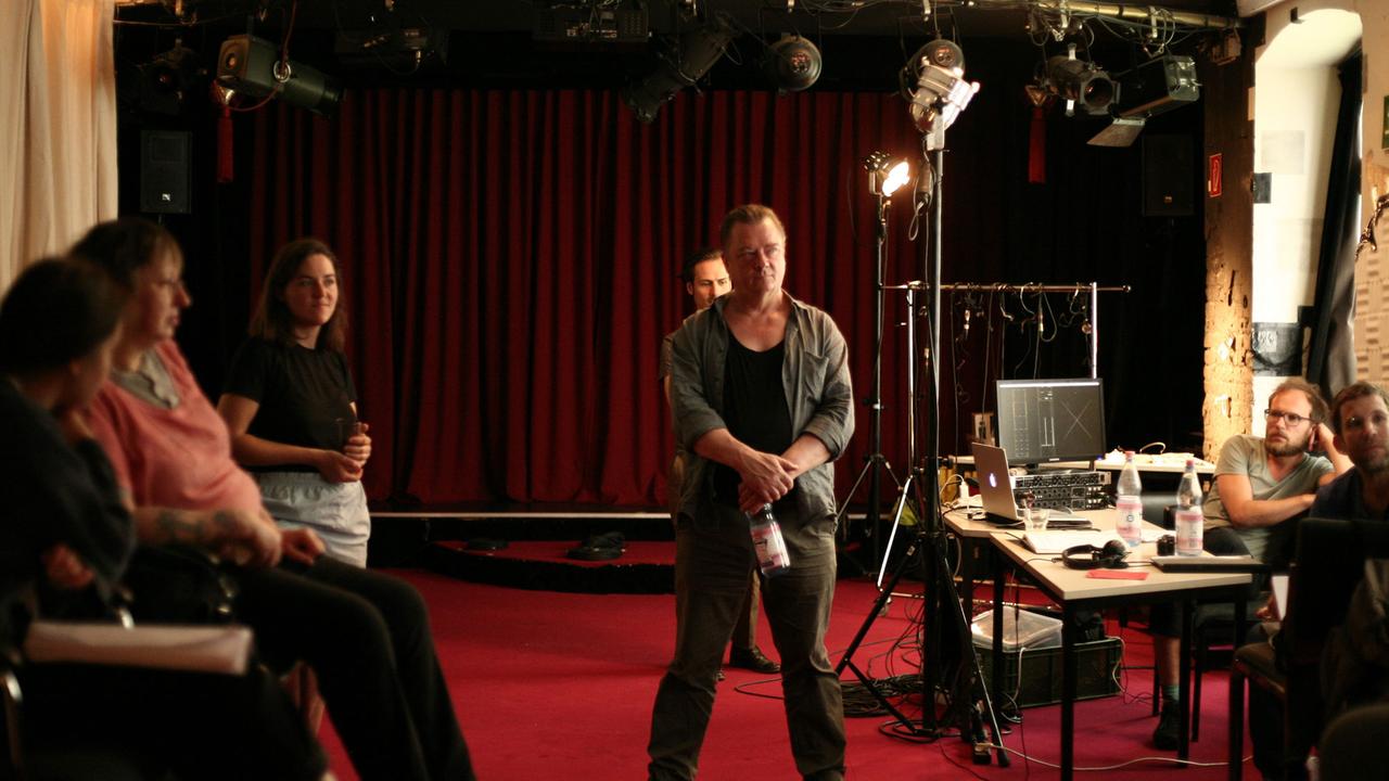 Studioaufnahmen für das Hörspiel "Der Absprung", mehrere Personen vor einer Bühne mit weinrotem Vorhang und einer Beleuchtungsschiene unter der Decke