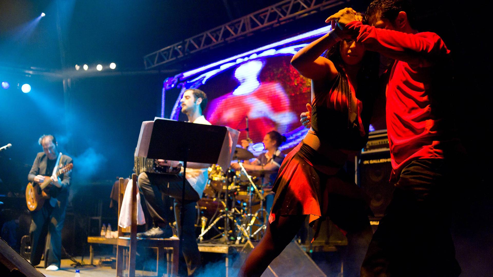 Die spanisch-argentinische Band Otros Aires ist bei einem Auftritt 2010 in Brasilien auf der Bühne zu sehen. Im Vordergrund tanzt ein Paar Tango. Die spanisch-argentinische Band Otros Aires ist bei einem Auftritt 2010 in Brasilien auf der Bühne zu sehen. Im Vordergrund tanzt ein Paar Tango.
