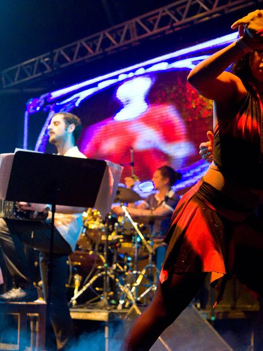 Die spanisch-argentinische Band Otros Aires ist bei einem Auftritt 2010 in Brasilien auf der Bühne zu sehen. Im Vordergrund tanzt ein Paar Tango.