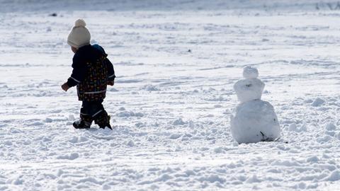 Ein Kleinkind hat einen Schneemann gebaut und geht von diesem weg.