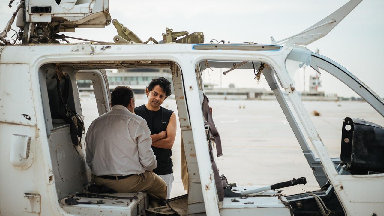 Naeem Mohaiemen steht auf dem verlassenen Flughafen "Athen Ellinikon" vor einem Helikopter, in dem Schauspieler sitzt. Naeem Mohaiemen steht auf dem verlassenen Flughafen "Athen Ellinikon" vor einem Helikopter, in dem Schauspieler sitzt.