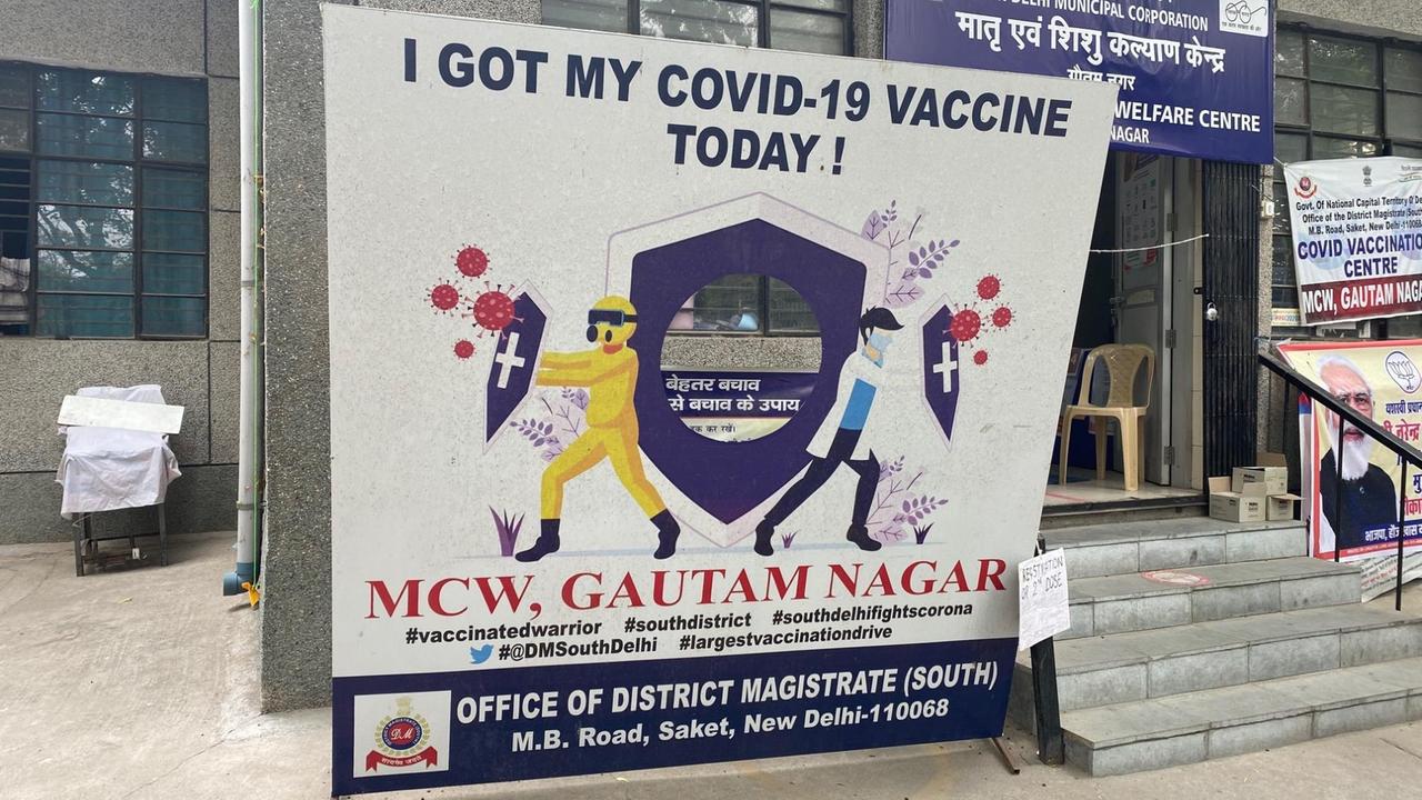 Vor einem Hauseingang steht ein großes Plakat, auf dem bunte Männchen mit Schildern das Coronavirus abwehren. Vor einem Hauseingang steht ein großes Plakat, auf dem bunte Männchen mit Schildern das Coronavirus abwehren.
