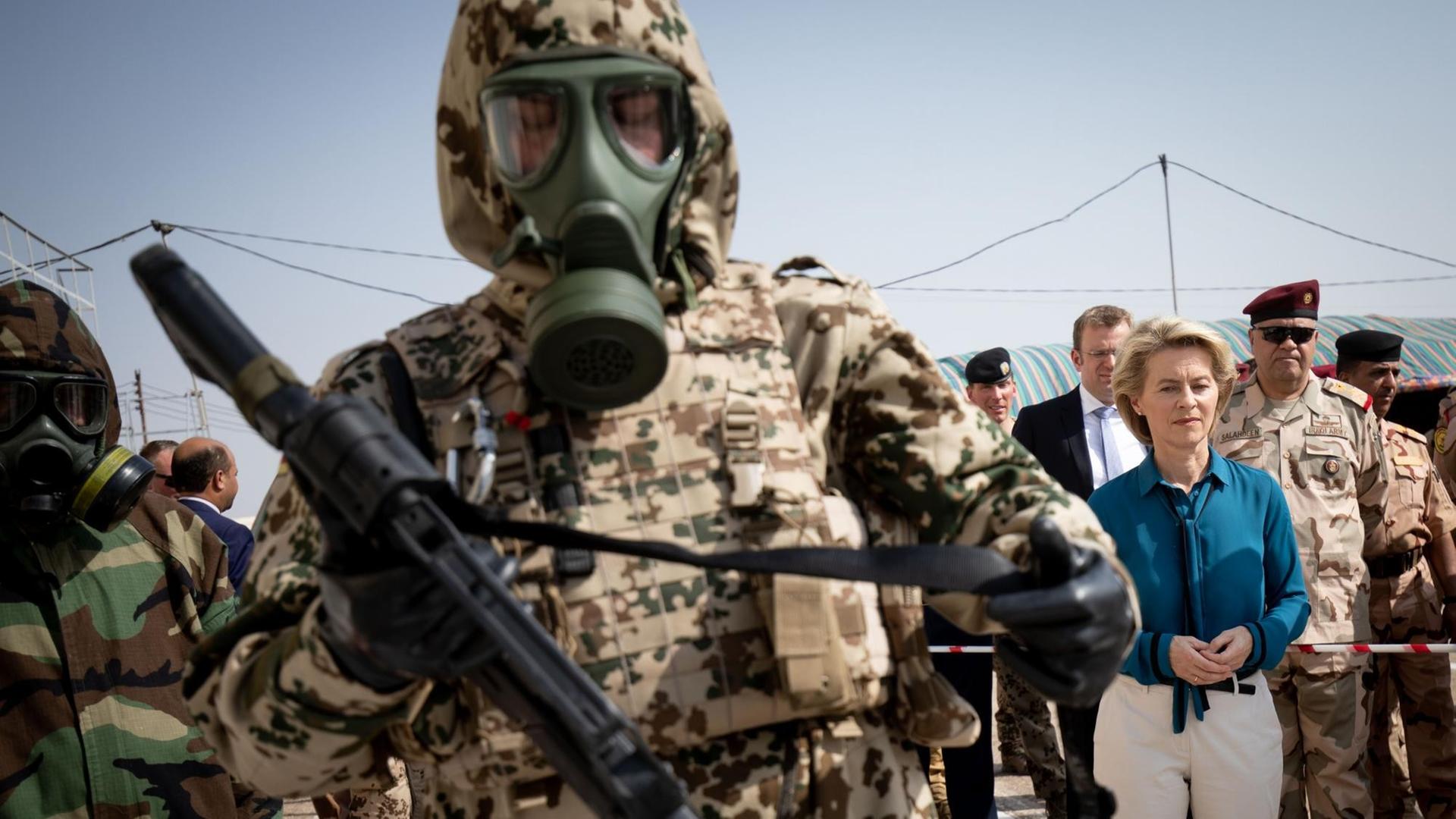 Bundesverteidigungsministerin Ursula von der Leyen steht beim Besuch im irakischen Armeestützpunkt Tadschi zwischen Bundeswehrsoldaten im Kampfanzug. Der Soldat im Vordergrund trägt eine Gasmaske. Bundesverteidigungsministerin Ursula von der Leyen steht beim Besuch im irakischen Armeestützpunkt Tadschi zwischen Bundeswehrsoldaten im Kampfanzug. Der Soldat im Vordergrund trägt eine Gasmaske.