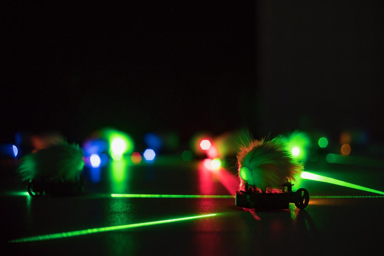 Ein mausartiger Roboter bewegt sich im Dunklen an einer Lichtbahn entlang. Ein mausartiger Roboter bewegt sich im Dunklen an einer Lichtbahn entlang.