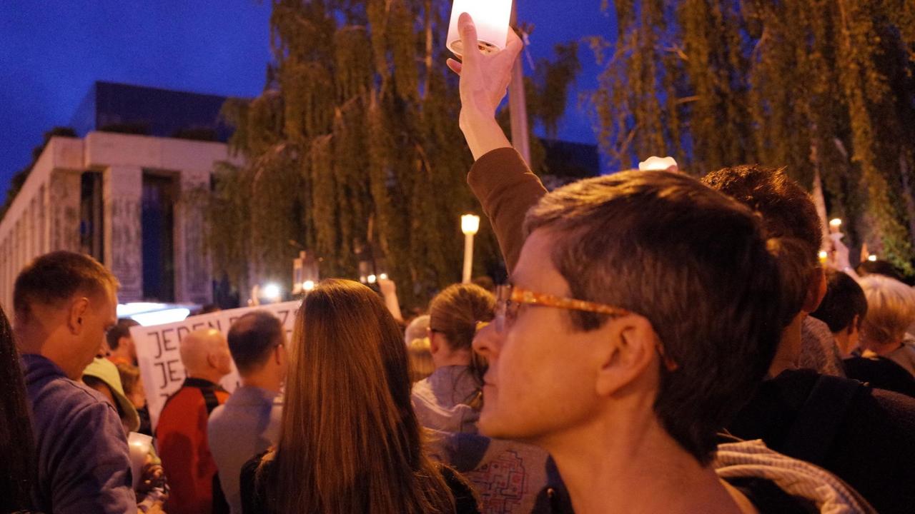 Eine Frau steht in einer Menschengruppe und hält eine Kerze hoch. Eine Frau steht in einer Menschengruppe und hält eine Kerze hoch.