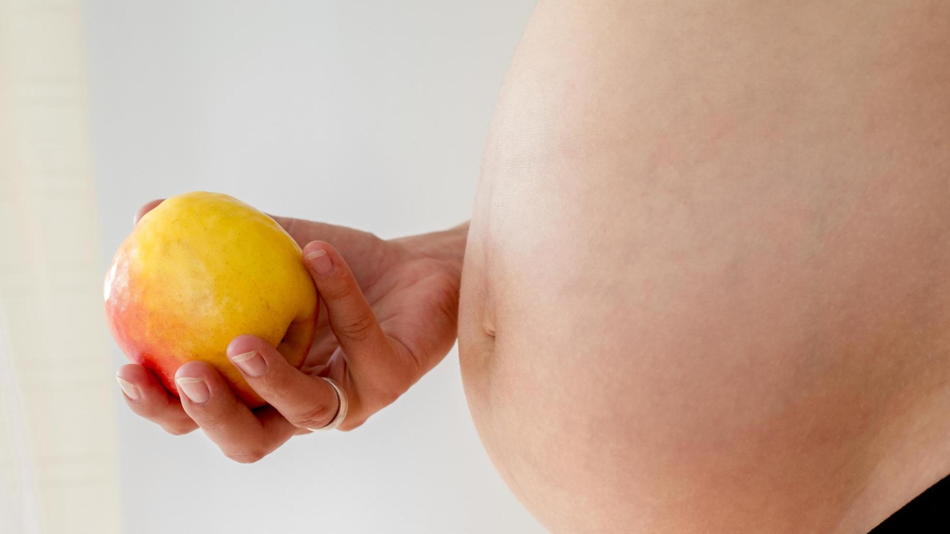 Eine schwangere Frau hält einen Apfel in der Hand.