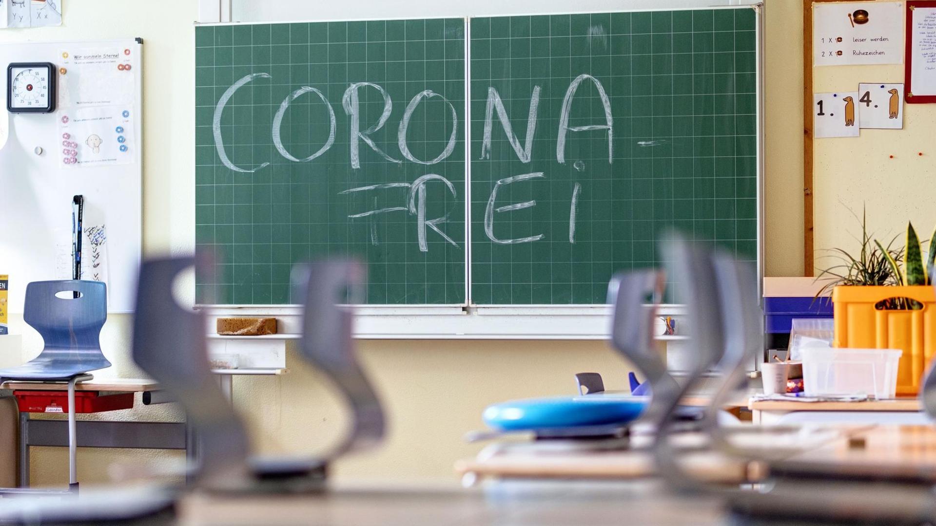 Corona-Frei steht auf einer Schultafel. Die Stühle im Raum sind hochgestellt auf die Tische. Corona-Frei steht auf einer Schultafel. Die Stühle im Raum sind hochgestellt auf die Tische.