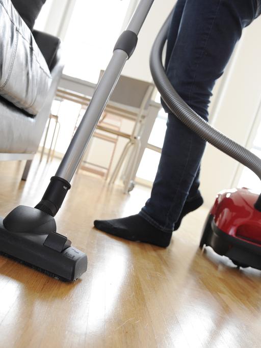 Eine Frau reinigt mit einem Staubsauger den Fußboden eines Wohnzimmers.