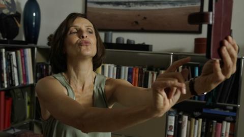 Filmszene aus "Match me if you can" mit Juliane Köhler: Sie hält ein Smartphone mit ausgestrecktem Arm von sich und versucht, ein Foto von sich mit Kussmund zu machen.