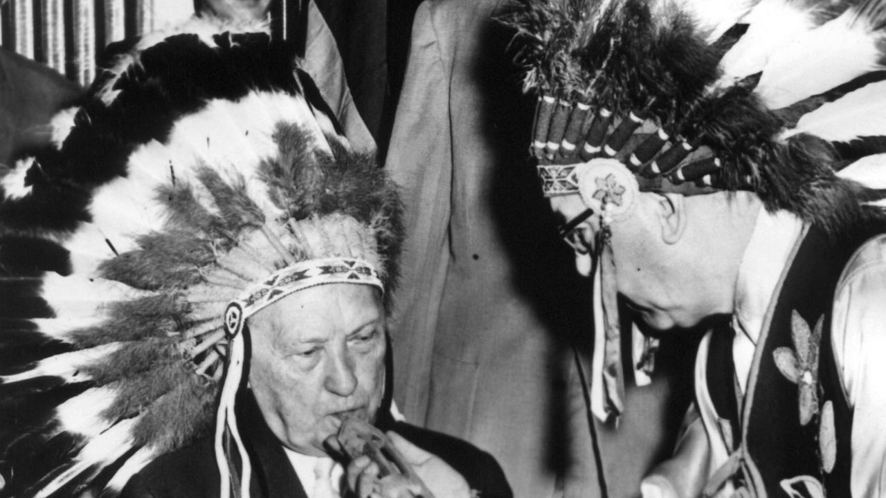 Der deutsche Bundeskanzler und Ehrenhäuptling Dr. Konrad Adenauer raucht am 16.6.1956 eine Friedenspfeife. Am letzten Tag seiner USA-Reise wurde Bundeskanzler Adenauer eine besondere Ehre zuteil: Er wurde zum Ehrenhäuptling der "Vereinigten Stämme der amerikanischen Indianer" ernannt.