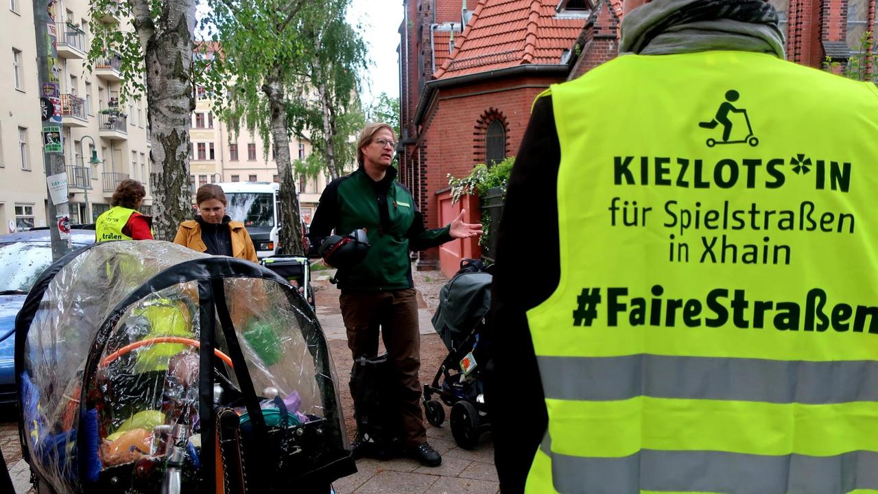 Amtsleiter Felix Weisbrich steht mit mehreren Menschen auf einer Straße. Eine Person trägt eine Warnweste mit der Aufschrift "Kiezlots*in für Spielstraßen in Xhain - #FaireStraßen." Amtsleiter Felix Weisbrich steht mit mehreren Menschen auf einer Straße. Eine Person trägt eine Warnweste mit der Aufschrift "Kiezlots*in für Spielstraßen in Xhain - #FaireStraßen."