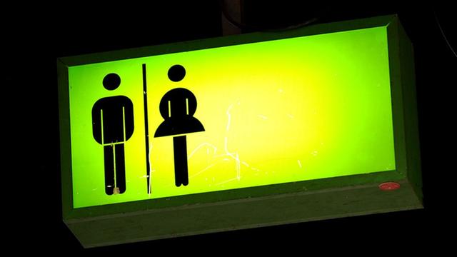 Auf einem grün leuchtendes Toiletten-Hinweisschild sind symbolisch die Figuren für Mann und Frau abgebildet.