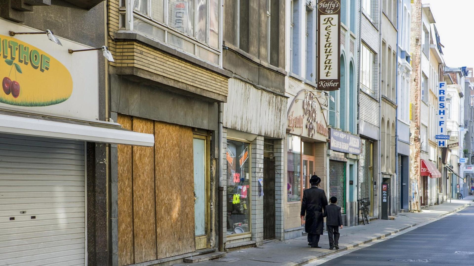 Ein jüdisch orthodoxer Mann mit schwarzem Mantel und Hut läuft mit einem Kind eine Straße entlang. Ein jüdisch orthodoxer Mann mit schwarzem Mantel und Hut läuft mit einem Kind eine Straße entlang.