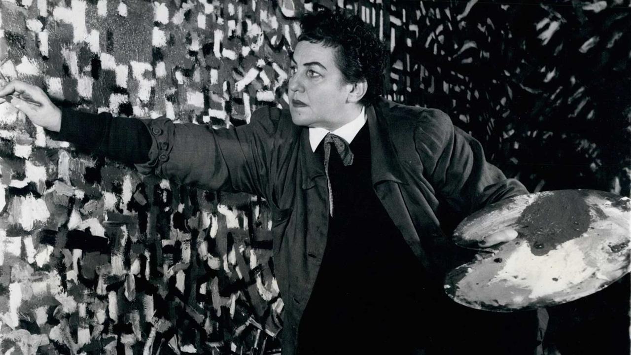 Auf einem Foto von 1962 hat sich die Malerin Fahrelnissa Zeid auf einen Stuhl gestellt, um die große Leinwand bemalen zu können. Auf einem Foto von 1962 hat sich die Malerin Fahrelnissa Zeid auf einen Stuhl gestellt, um die große Leinwand bemalen zu können.