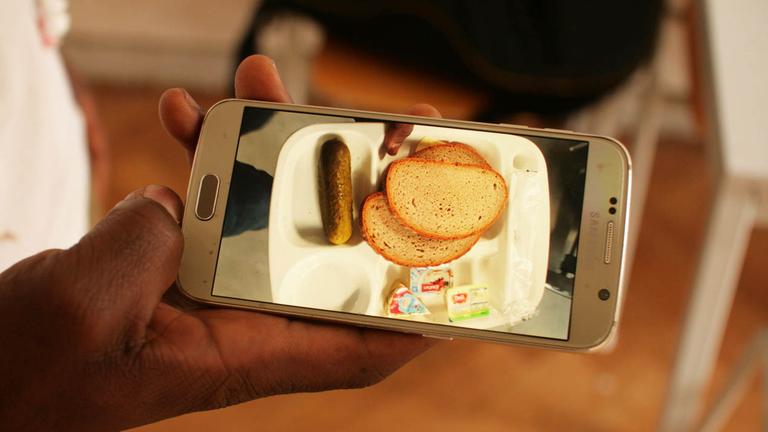 Zwei Scheiben Brot, ein bisschen Butter: das Abendessen in der Unterkunft - Arona zeigt ein Bild von der Mahlzeit auf seinem Handy. Zwei Scheiben Brot, ein bisschen Butter: das Abendessen in der Unterkunft - Arona zeigt ein Bild von der Mahlzeit auf seinem Handy.