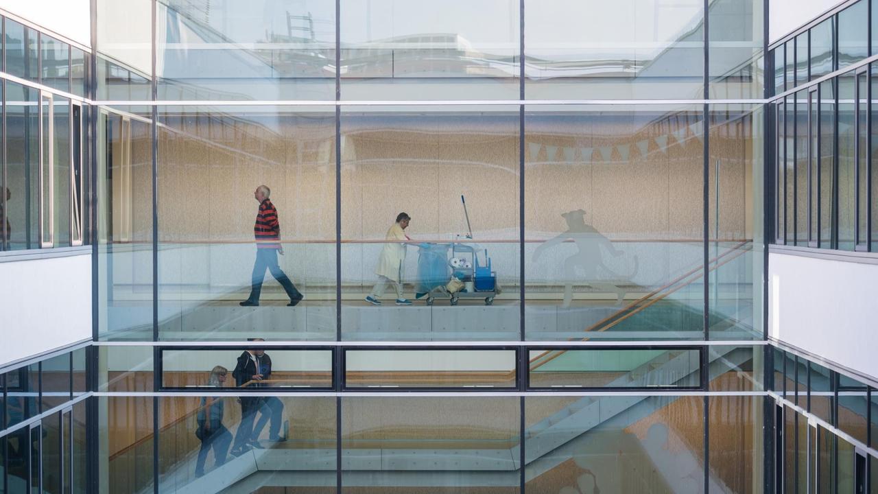 Besucher und eine Reinigungskraft gehen am durch einem verglasten Durchgang im Universitätsklinikum Frankfurt in Frankfurt am Main (Hessen). Besucher und eine Reinigungskraft gehen am durch einem verglasten Durchgang im Universitätsklinikum Frankfurt in Frankfurt am Main (Hessen).