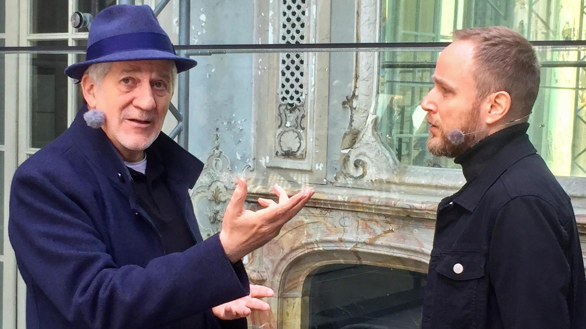 Ilja Richter schaut in die Kamera, während er mit Olaf Kosert spricht. Im Hintergrund ein eingerüstetes Haus mit beschädigter Fassade. Ilja Richter schaut in die Kamera, während er mit Olaf Kosert spricht. Im Hintergrund ein eingerüstetes Haus mit beschädigter Fassade.